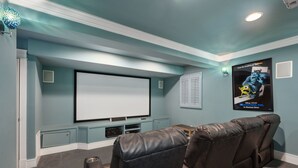 A home theater room with a large flat-screen TV, leather reclining chairs, and a poster on the wall.