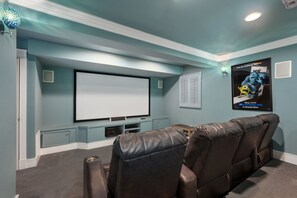 A home theater room with a large flat-screen TV, leather reclining chairs, and a poster on the wall.