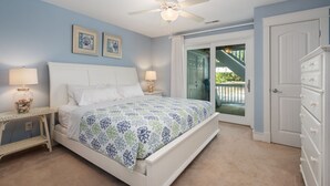 A bedroom with a bed, two bedside lamps, a ceiling fan, and a door leading to a balcony.