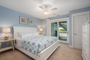 A bedroom with a bed, two bedside lamps, a ceiling fan, and a door leading to a balcony.