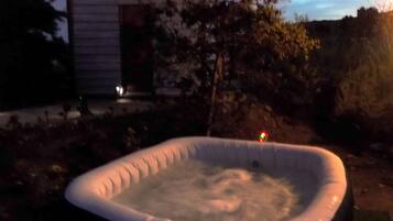 An outdoor hot tub surrounded by trees and a building.