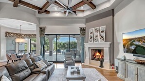 Un amplio salón con sofá de cuero, chimenea, televisor y comedor con vistas al exterior.