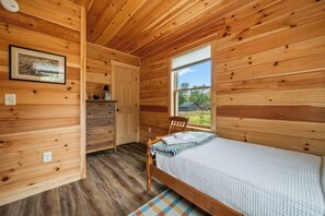 A wooden cabin bedroom with a bed, a chair, a dresser, a window, and a framed picture on the wall. - Niboban Cabin 17 - shared waterfront (Rangeley)