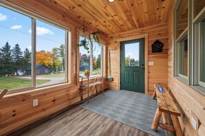 A wooden cabin interior with large windows, a green door, a bench, and a hanging plant.