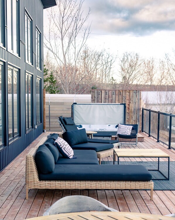 Une terrasse extérieure moderne, dotée d’un canapé de couleur foncée, de deux fauteuils, d’une petite table et d’un ventilateur de plafond.