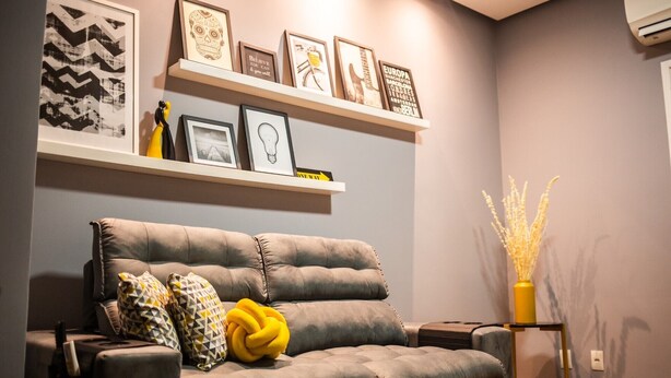 Una sala de estar con un sofá gris, cojines estampados y una mesita de vidrio con un jarrón amarillo.