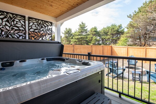 A hot tub on a covered deck with a wooden fence and outdoor seating in the background.
