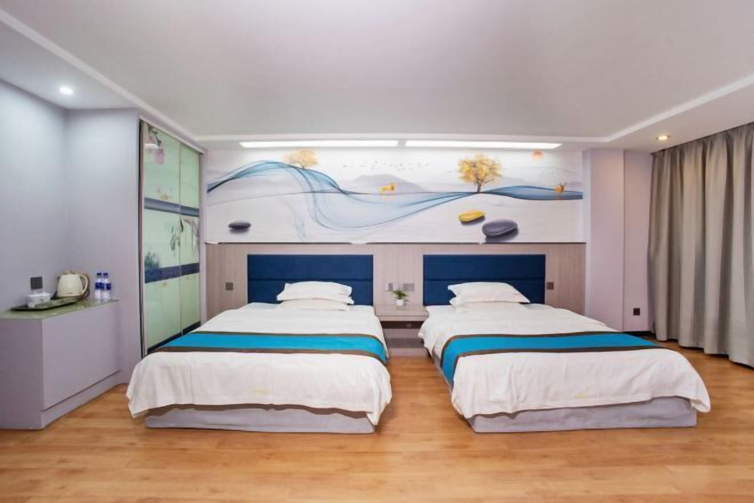 Una habitación de hotel con dos camas, un escritorio con lámpara y un mural en la pared.