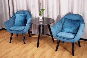Zwei blaue Samt-Sessel mit schwarzen Beinen, ein kleiner runder Tisch und ein Blumentopf.