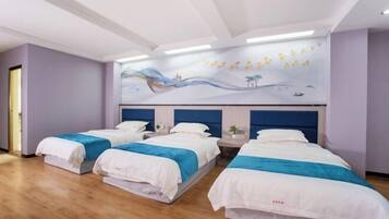 Habitación de hotel con tres camas, cada una con ropa de cama blanca y detalles azules. El piso es de madera, hay un mural grande en la pared que representa un paisaje tranquilo y un diseño de techo moderno con iluminación empotrada.