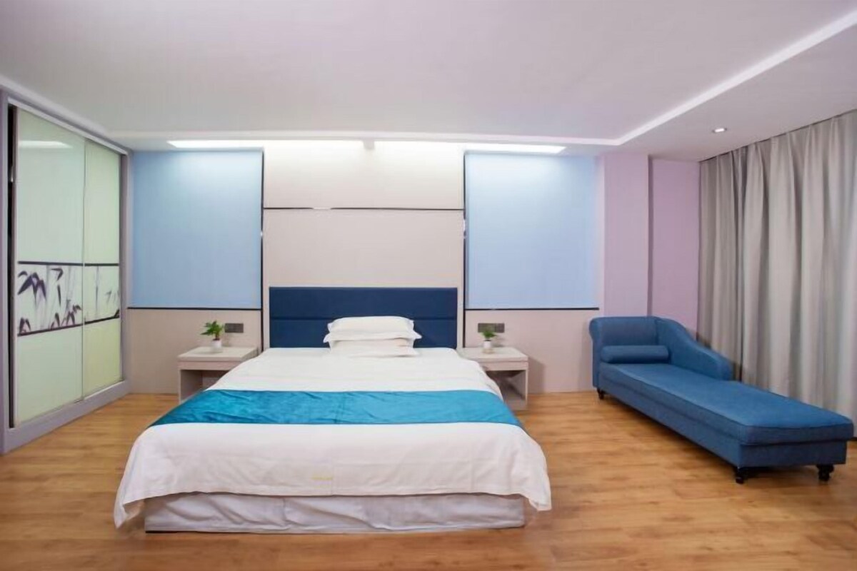 Ein Hotelzimmer mit einem Bett, einem Nachttisch, einer blauen Couch und einem großen Fenster mit Vorhängen.