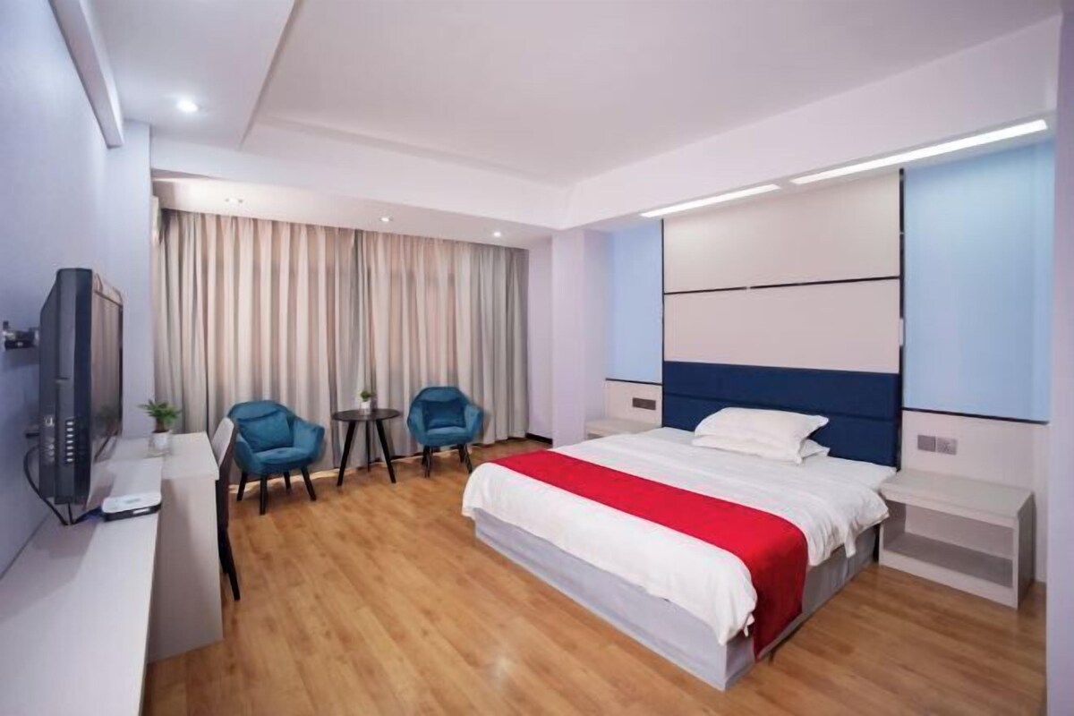 Ein modernes Hotelzimmer mit Bett, zwei Stühlen, einem Schreibtisch, einem Fernseher und einem großen Spiegel.