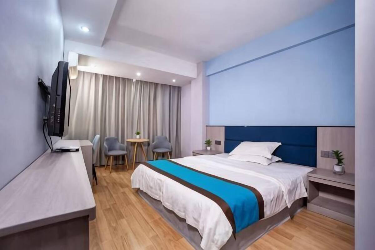 Moderni hotellihuone, jossa on sänky, työpöytä, tuoli, pieni pöytä ja televisio.