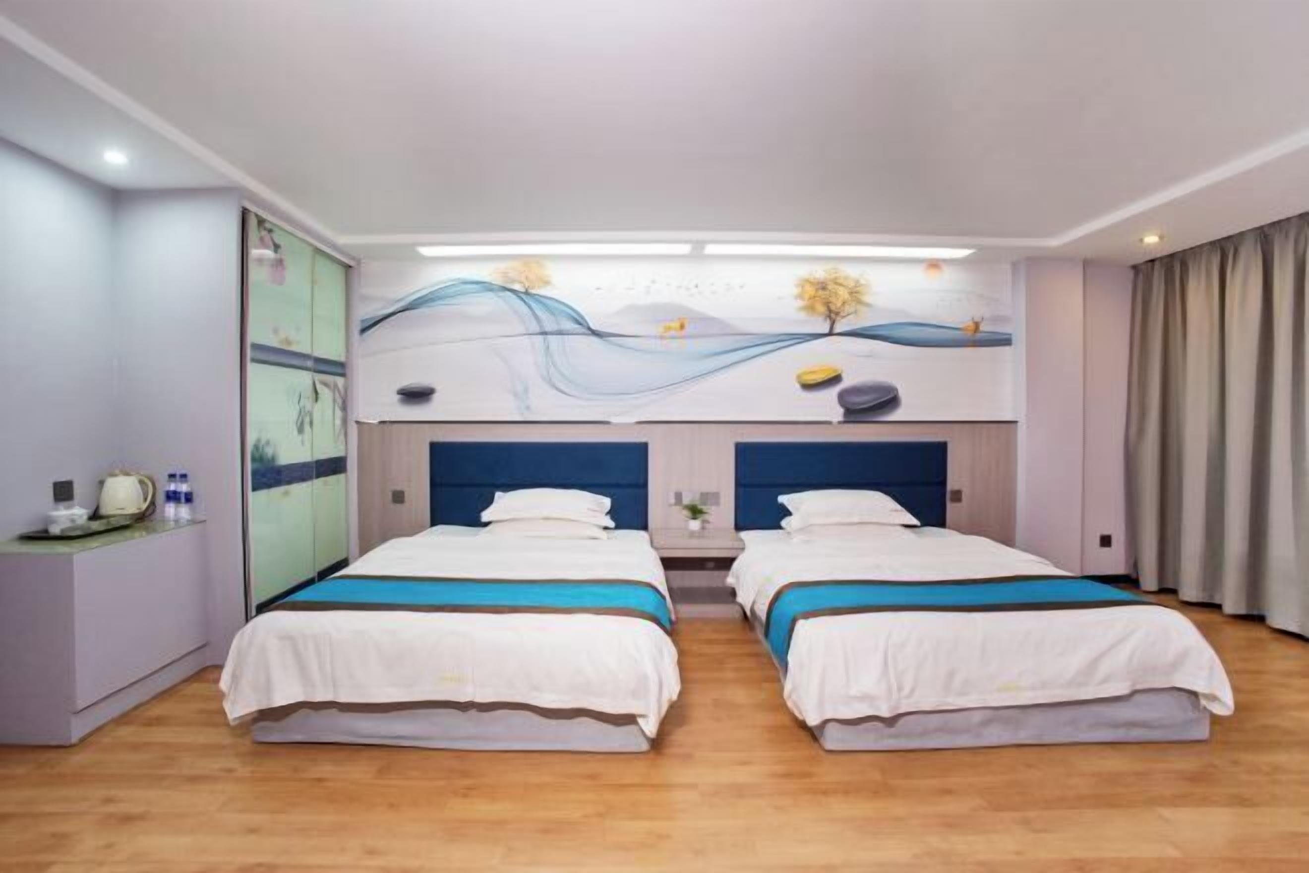Habitación de hotel con dos camas, un escritorio con lámpara y un mural en la pared.