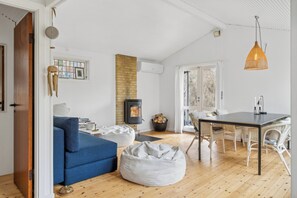 A living room with a sofa, bean bag, dining table, wicker chairs, a fireplace, and a hanging light fixture.