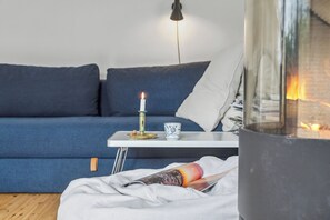 A cozy room with a blue sofa, a white table with a candle, and a glass fireplace.