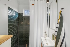 A bathroom with a tiled shower, a sink, and a mirror.