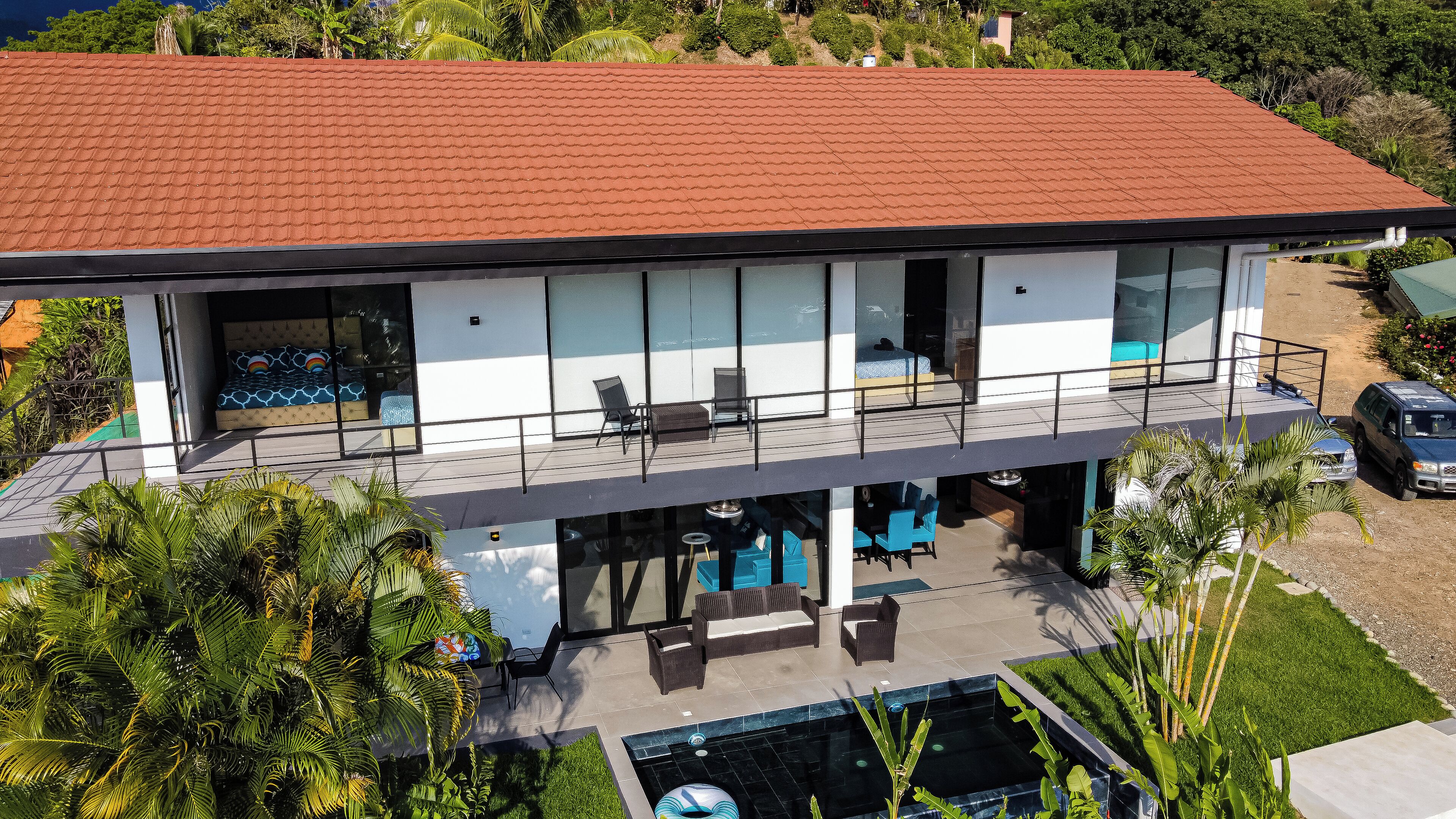A modern two-story house with a red-tiled roof, large glass windows, and a swimming pool.