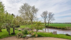 A landscaped garden with a pond, trees, and a grassy field. - Gardiners Cottage Barn, Eye (Stoke Ash)
