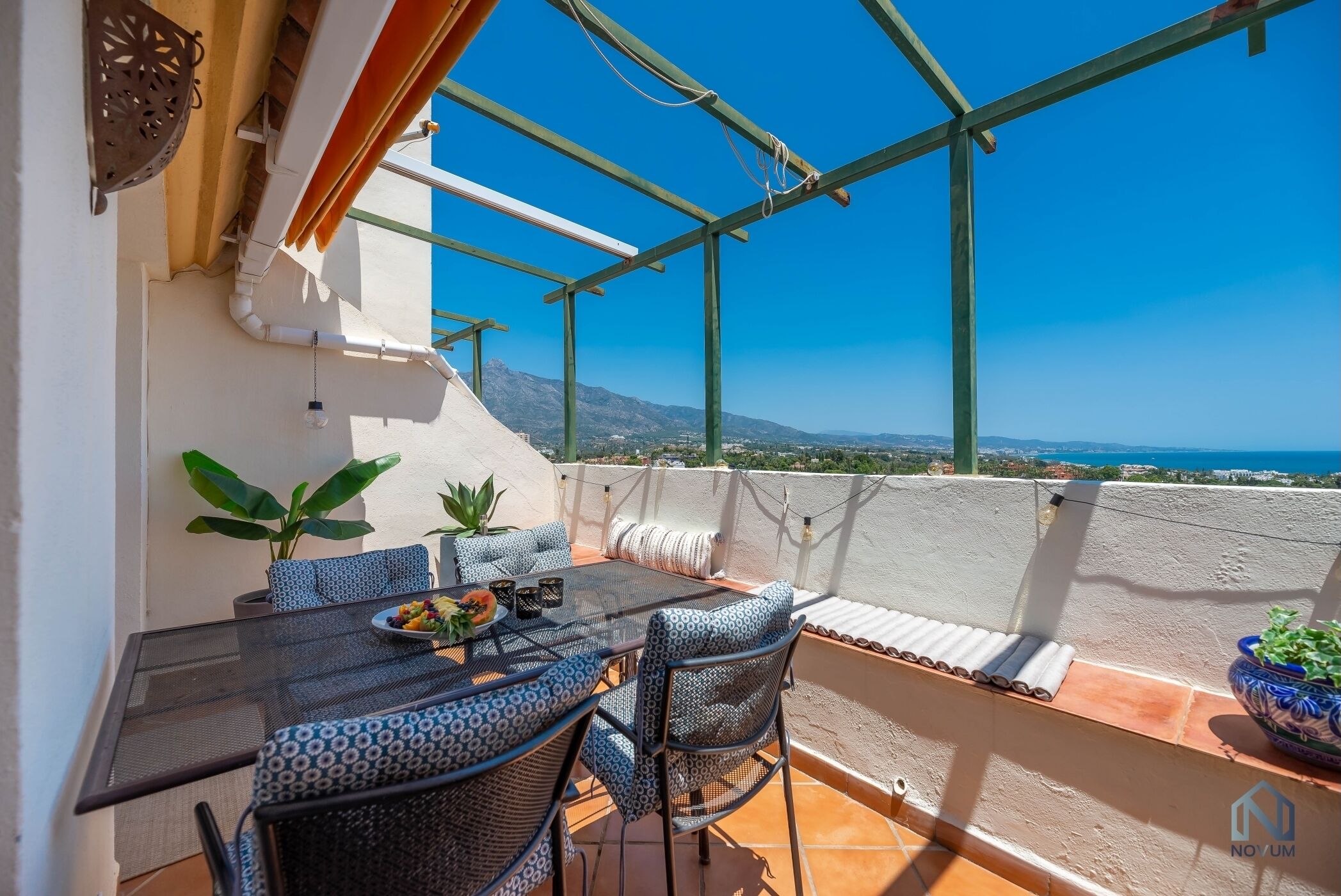 Eine Terrasse mit Tisch, Stühlen, einer Topfpflanze und Blick auf die Landschaft.