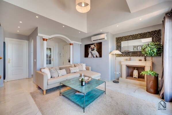 A modern living room with a beige sofa, a glass coffee table, and a fireplace.