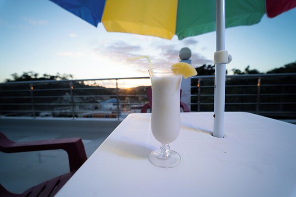 A tall glass of a white beverage with a straw and a slice of fruit on a white table under a colorful umbrella.