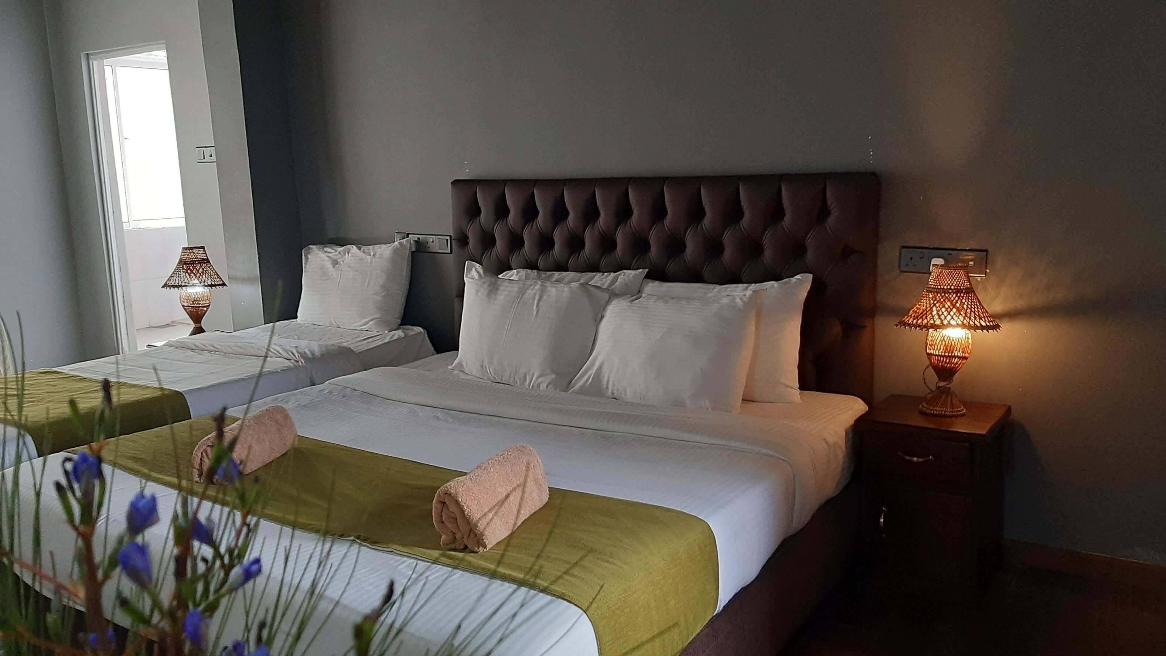 A hotel room with two beds, a tufted headboard, bedside lamps, and a window with natural light.