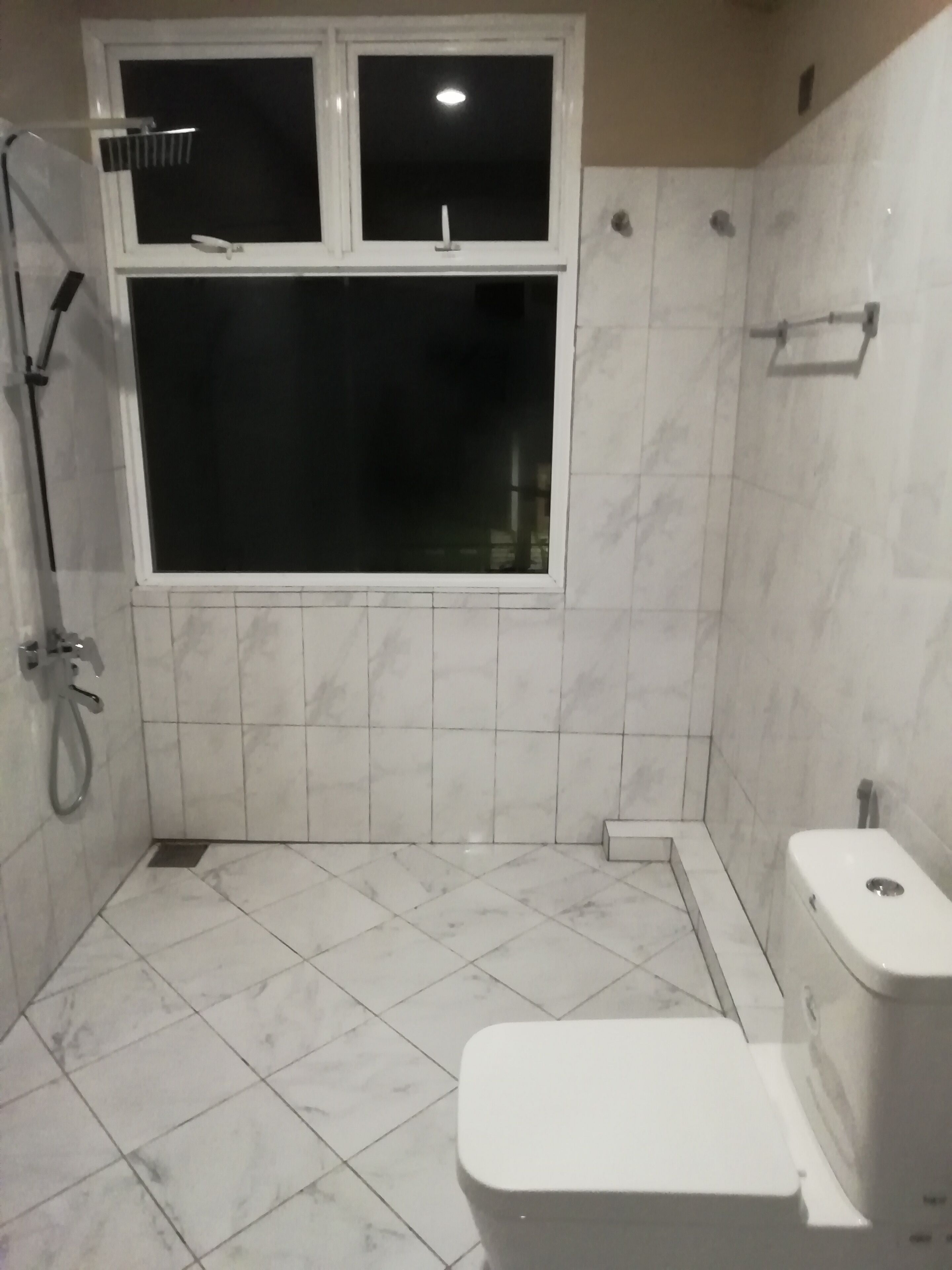 A small, tiled bathroom with a toilet, a shower, and a window.