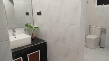 Une salle de bain moderne avec un lavabo blanc, un miroir, une petite plante en pot et des toilettes.