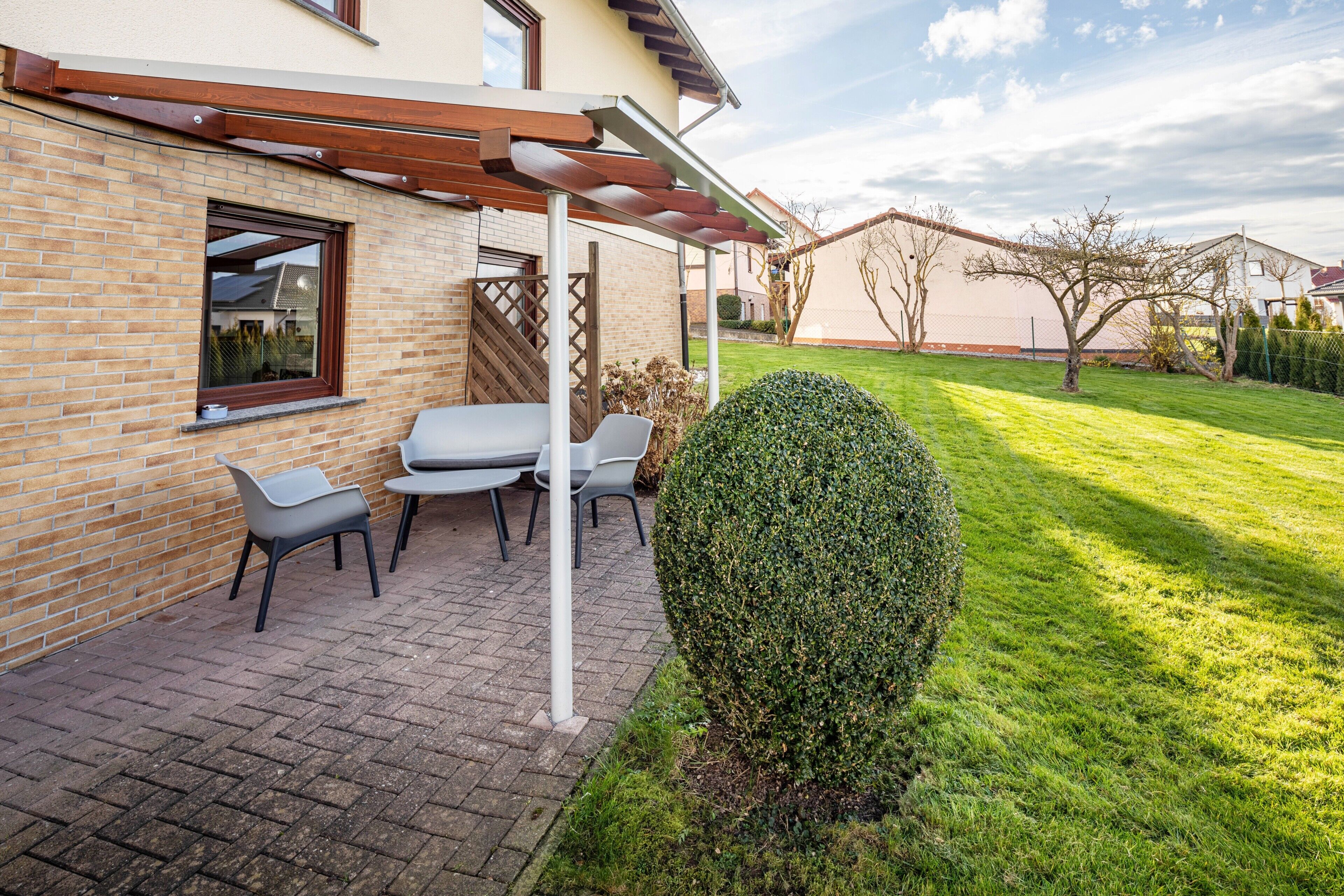 Eine Terrasse mit einer Pergola, einer Backsteinmauer und einem gepflegten Rasen.