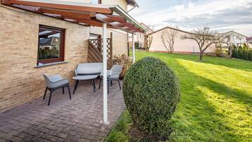 Eine Terrasse mit einer Pergola, einer Backsteinmauer und einem gepflegten Rasen.
