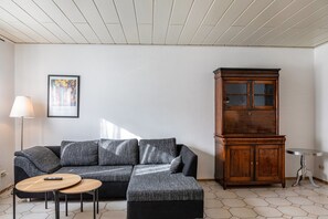 Un salon comprenant un canapé d’angle, un meuble en bois, une lampe et une petite table ronde.