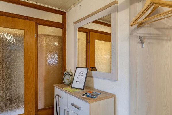 A room with a wooden cabinet, a framed sign, a small table, and a mirror on the wall.