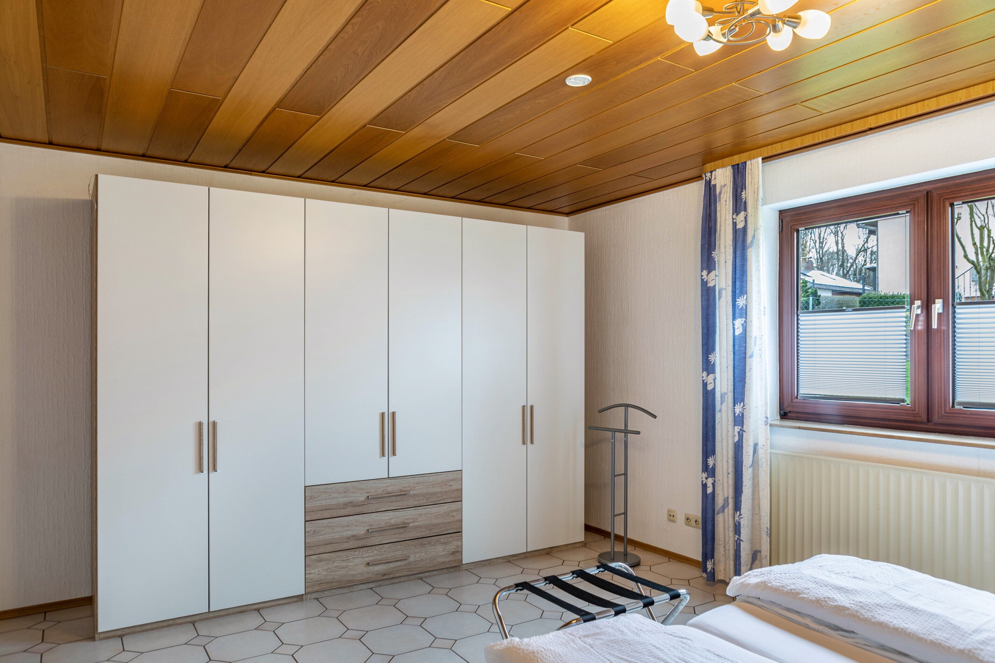 Ein Schlafzimmer mit Kleiderschrank, Bett, Heizkörper und einem Fenster mit Jalousien.