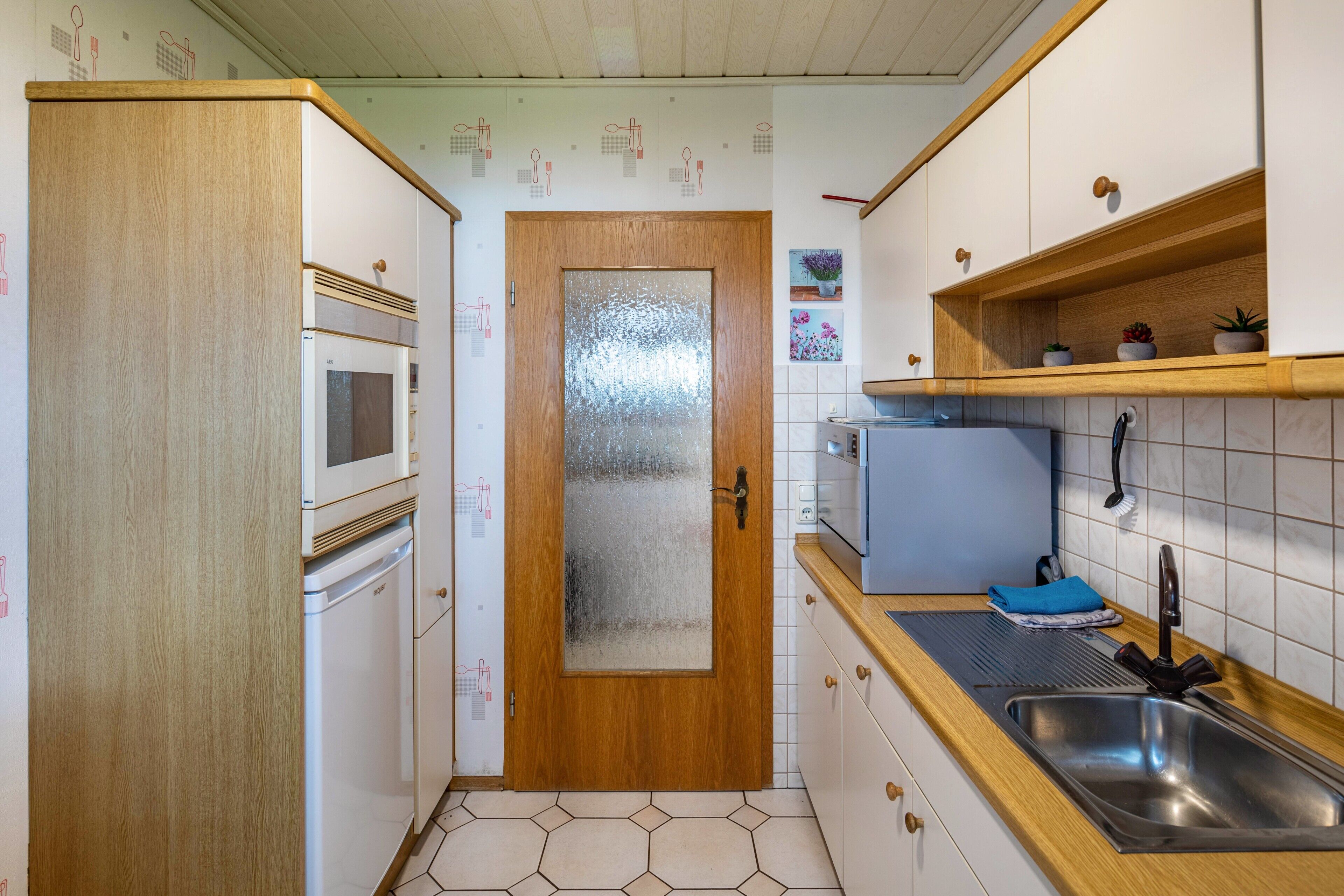 A compact kitchen with a wooden door, white cabinets, a stainless steel sink, and a microwave.