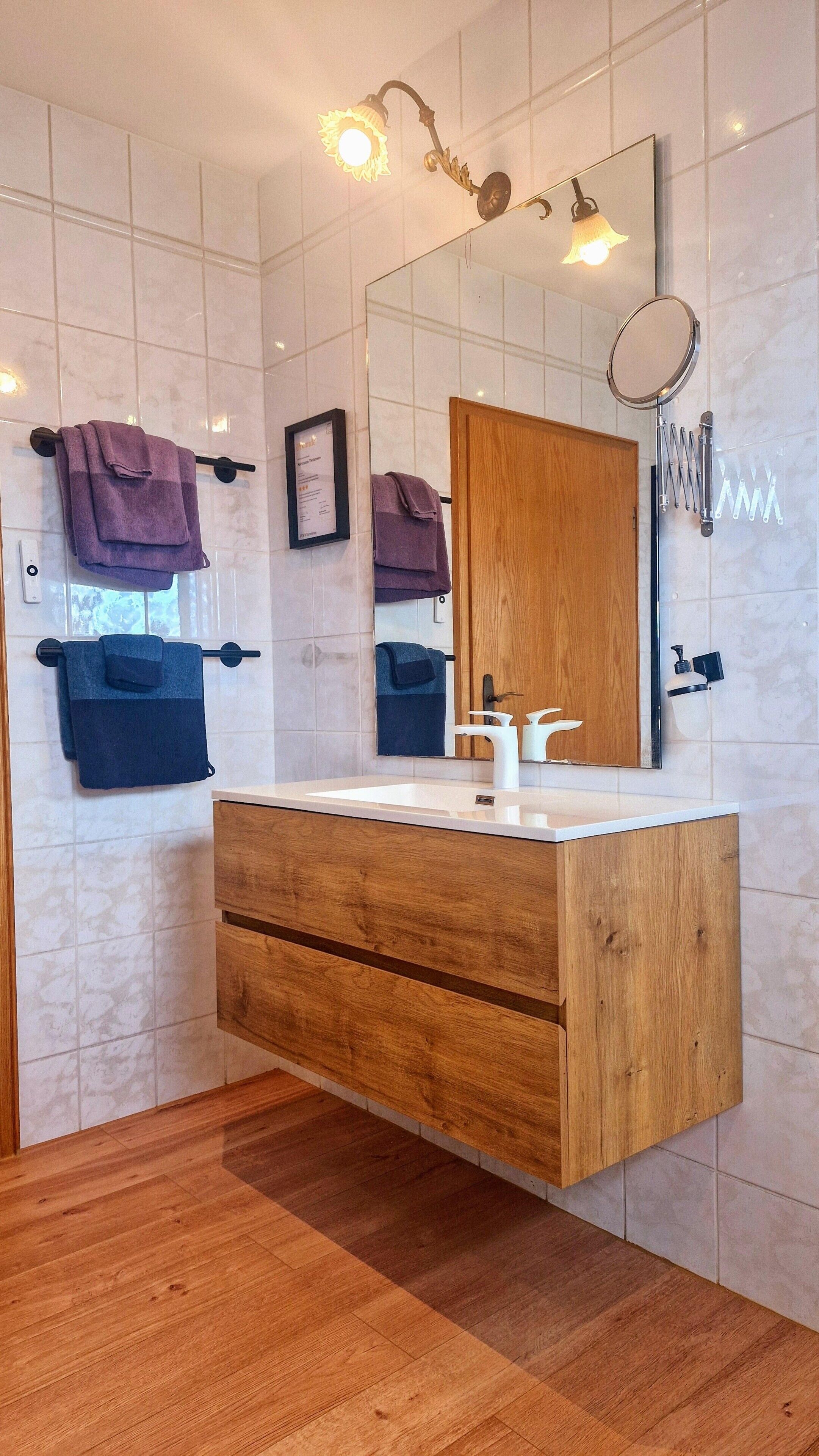 A bathroom with a wooden vanity, a mirror, a towel rack, and a shower with a handheld showerhead.