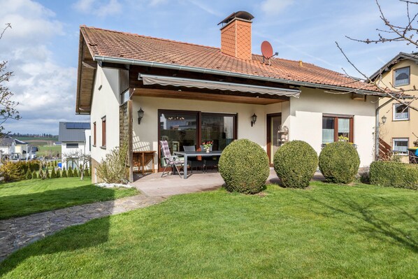 Une maison à deux étages, avec un toit en tuiles, une terrasse couverte et une pelouse bien entretenue.