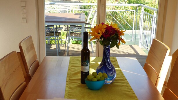 Ein Esstisch mit Papier, einer Flasche, einer Blumenvase und einer Fruchtschale.