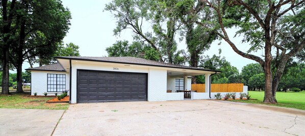 Einbungalow mit Garage, umgeben von Bäumen und einem gepflegten Rasen.