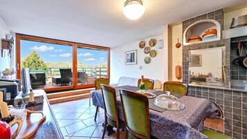 A dining area with a table set for four, a kitchen with modern appliances, and a large window offering a view of greenery.