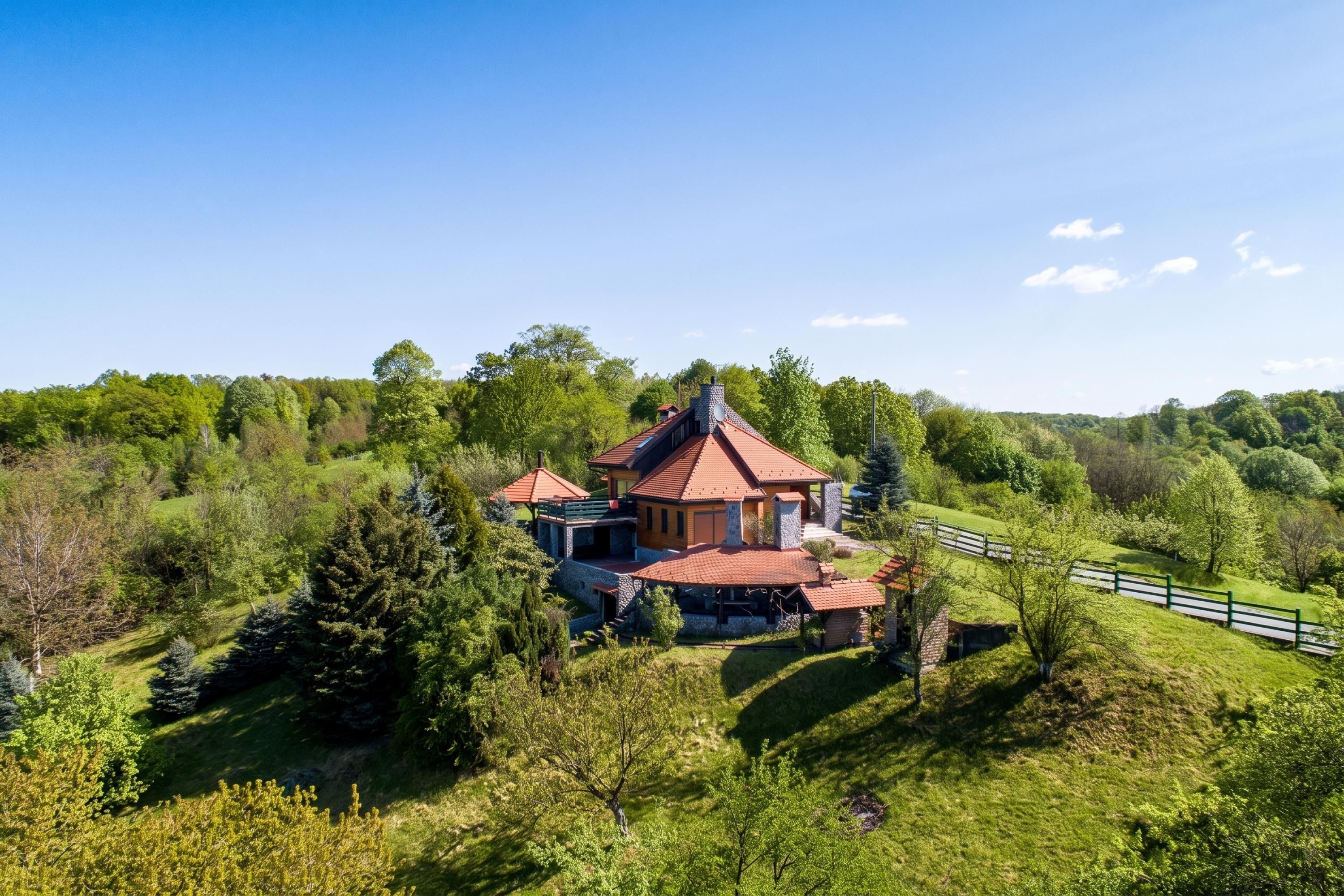 Une grande maison avec un toit rouge, entourée d’une végétation luxuriante et d’arbres.