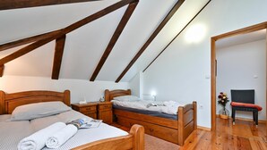 A bedroom with a sloped ceiling, wooden beams, a bed with pillows, a nightstand, a dresser, and a chair.