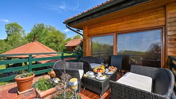 A wooden deck with outdoor furniture, a table set for breakfast, and a view of the surrounding greenery.