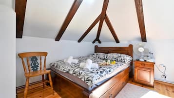 A bedroom with a wooden bed, a wooden chair, a nightstand with a fan, and a dresser.