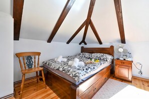 A bedroom with a wooden bed, a wooden chair, a nightstand with a fan, and a dresser.