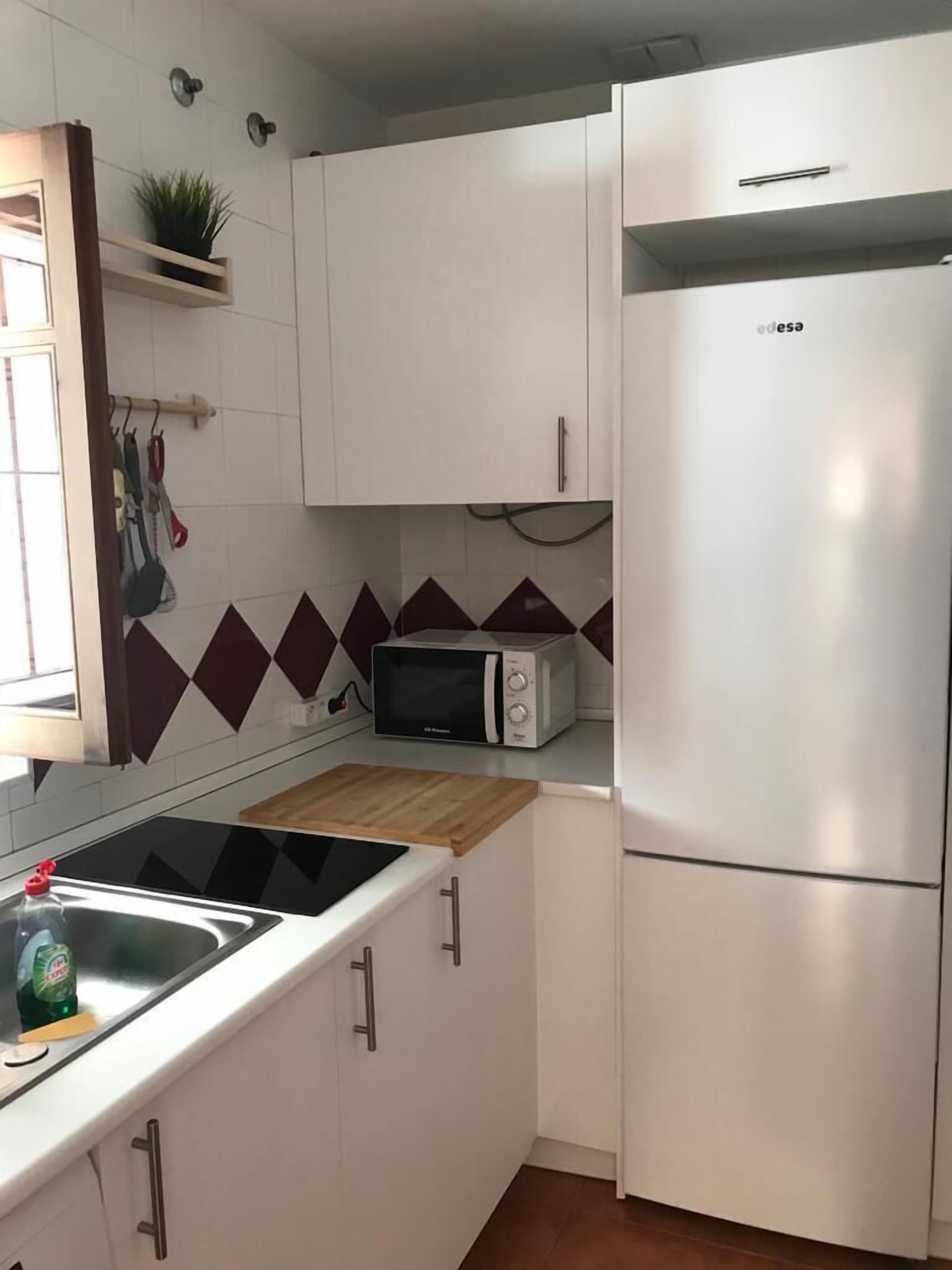 A kitchen with white cabinets, a microwave, a refrigerator, a wooden countertop, and a sink with dish soap.