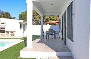 Relax in an outdoor space with a pool and lawn, surrounded by a covered patio with a table and chairs.