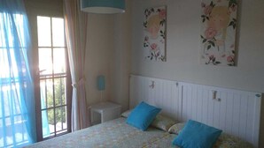 A bedroom with a bed, a nightstand, a window with curtains, and floral wall art. - Apartment Los Pelicanos (Ayamonte)