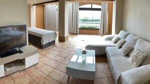 A living room with a TV, a sofa, a coffee table, and a balcony with curtains. - Apartment Los Pelicanos (Ayamonte)