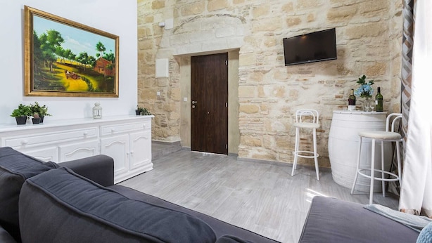 A living room with a stone wall, a TV mounted above a door, a sofa, and a small bar area with stools.